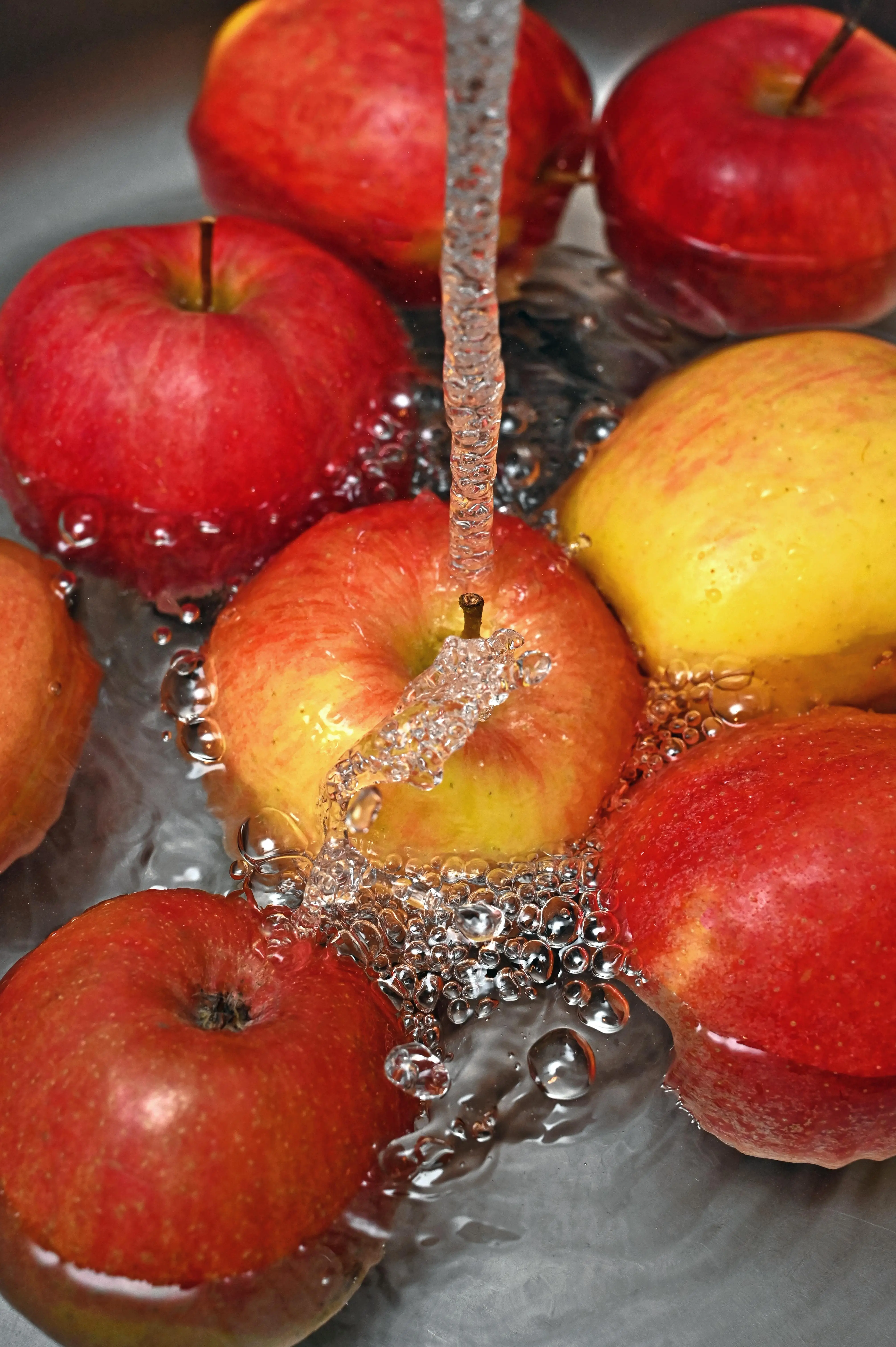 Fresh whole apples being rinsed under running water, representing clean nutrition and whole-food wellness as part of Mind & Body Infusions' holistic health approach