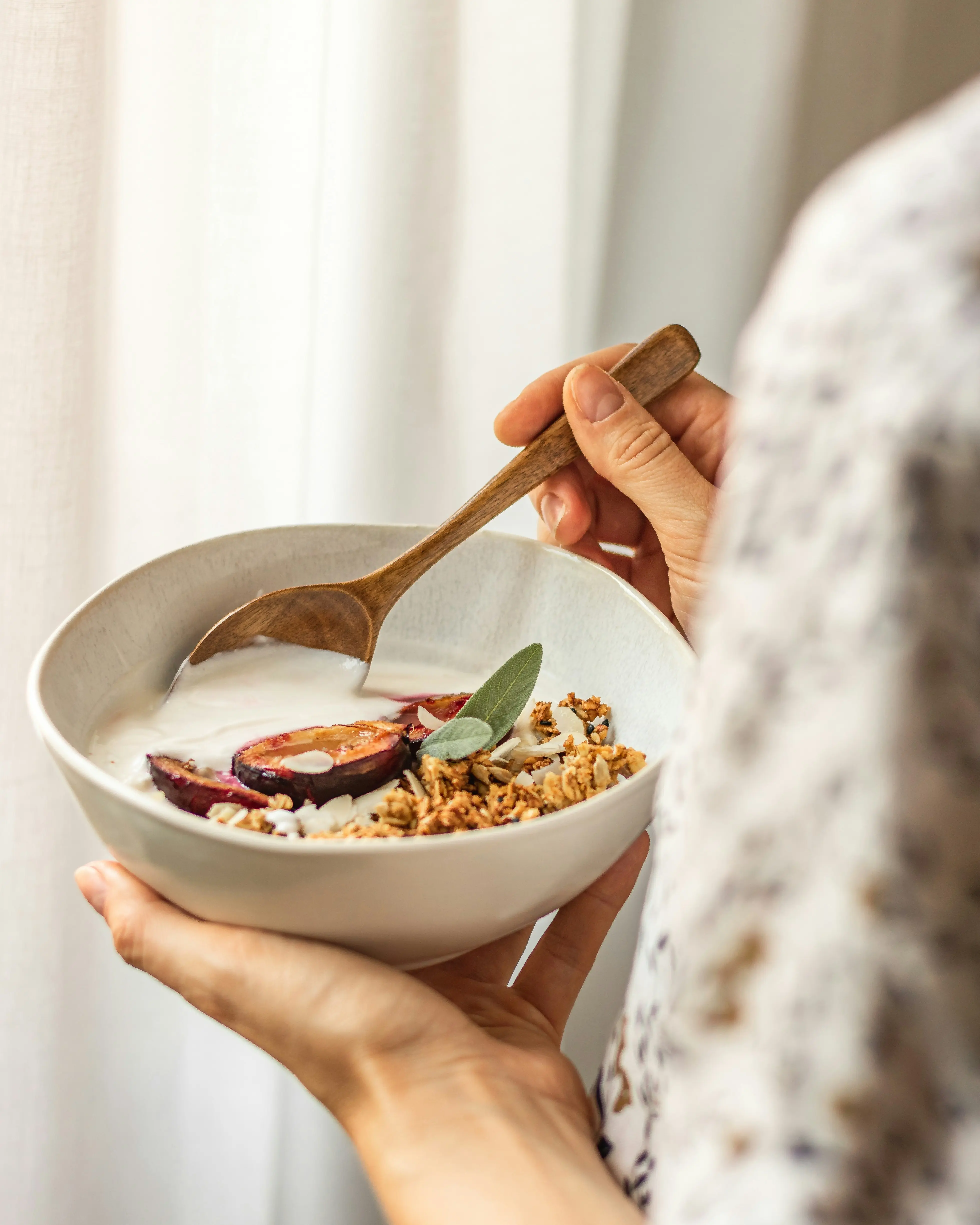 Person holding a nourishing wellness bowl with granola, roasted fruit, and yogurt, representing Mind & Body Infusions' integrative approach to nutrition and holistic health