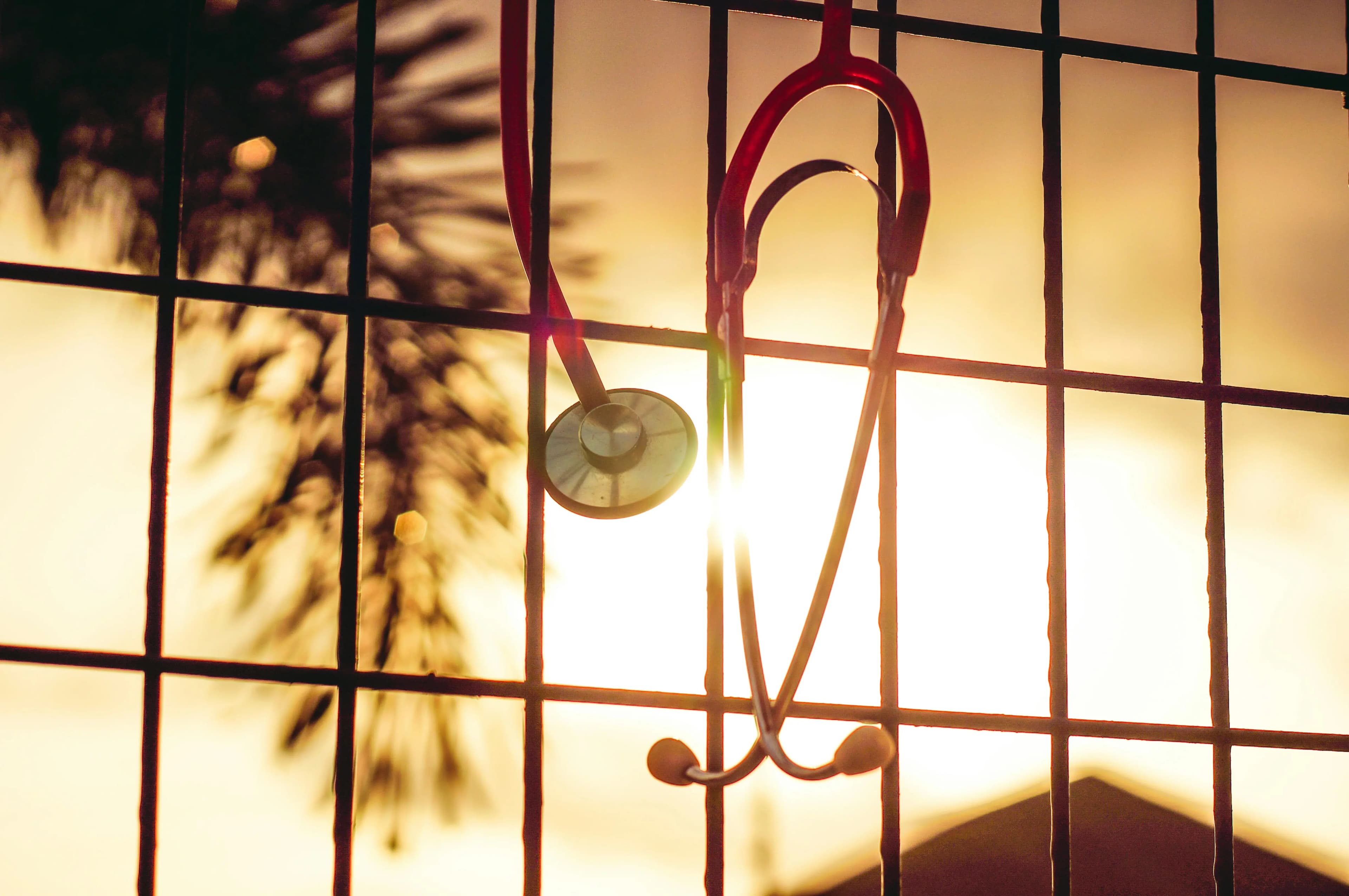 Stethoscope hanging on a metal fence against a golden sunset sky, representing Mind & Body Infusions' comprehensive integrative health and wellness services
